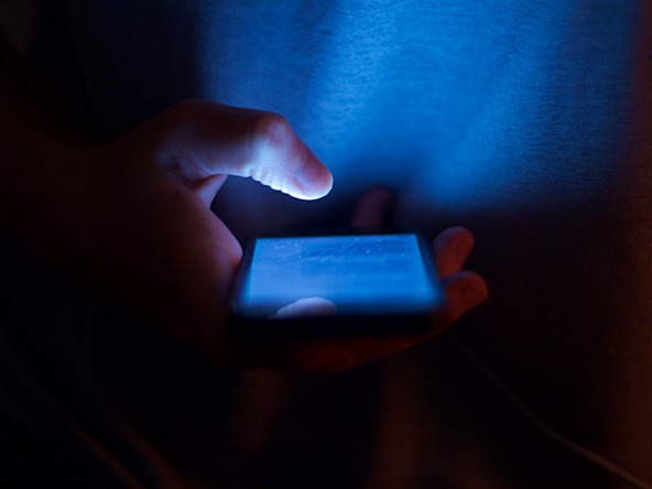 Someone scrolling through a blue mobile phone in the dark